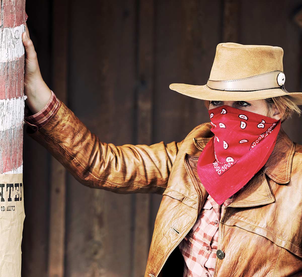 Bad Cow Girl with bandana to mask face learning against a post